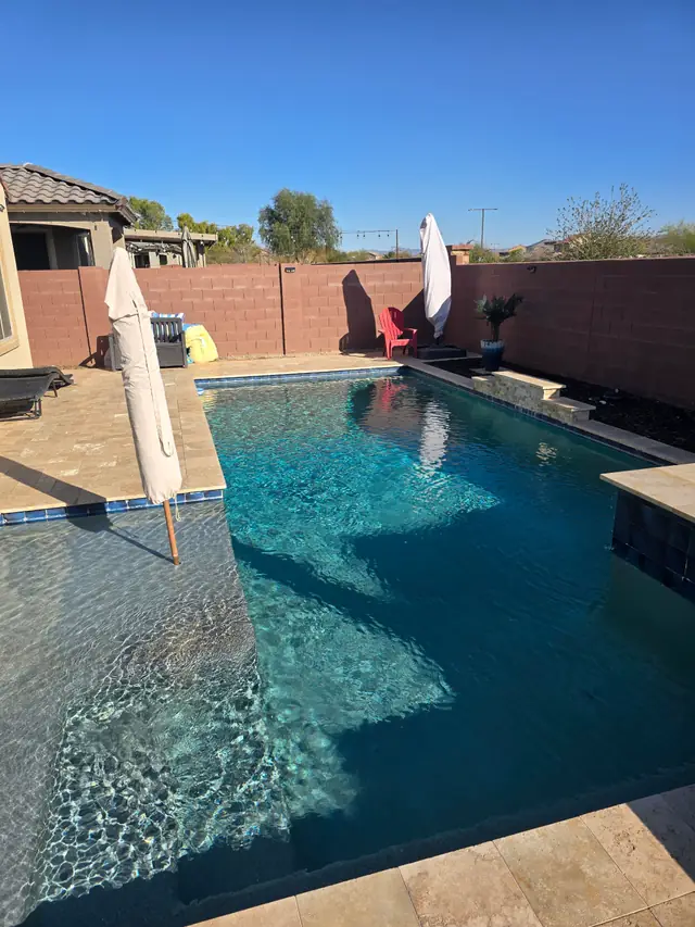 Clear blue water over a tanning ledge with travertine coping and a block wall in Surprise