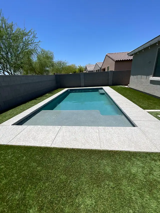 Rectangular pool with a sun shelf, artificial turf and a gray block wall